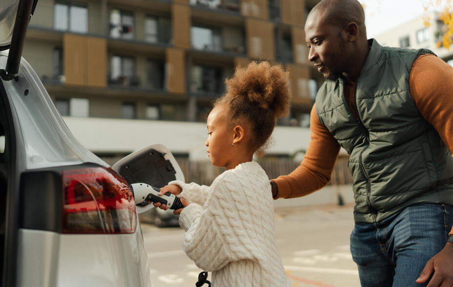 A father helps his daughter connect their electric vehicle to a charging cable.