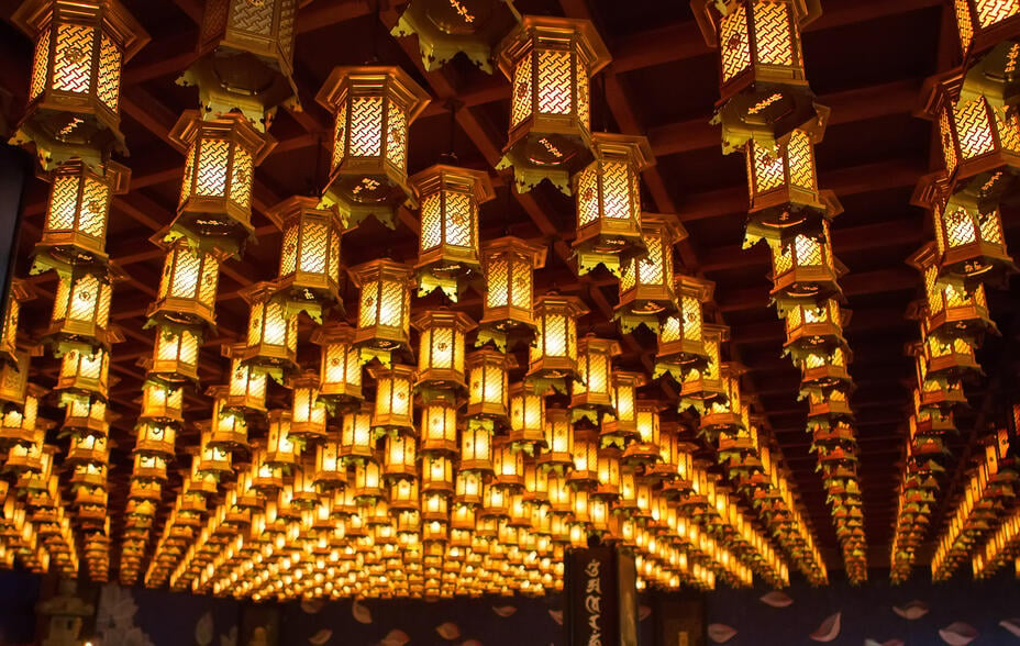 Hundreds of lit lanterns are hanging together from a temple ceiling