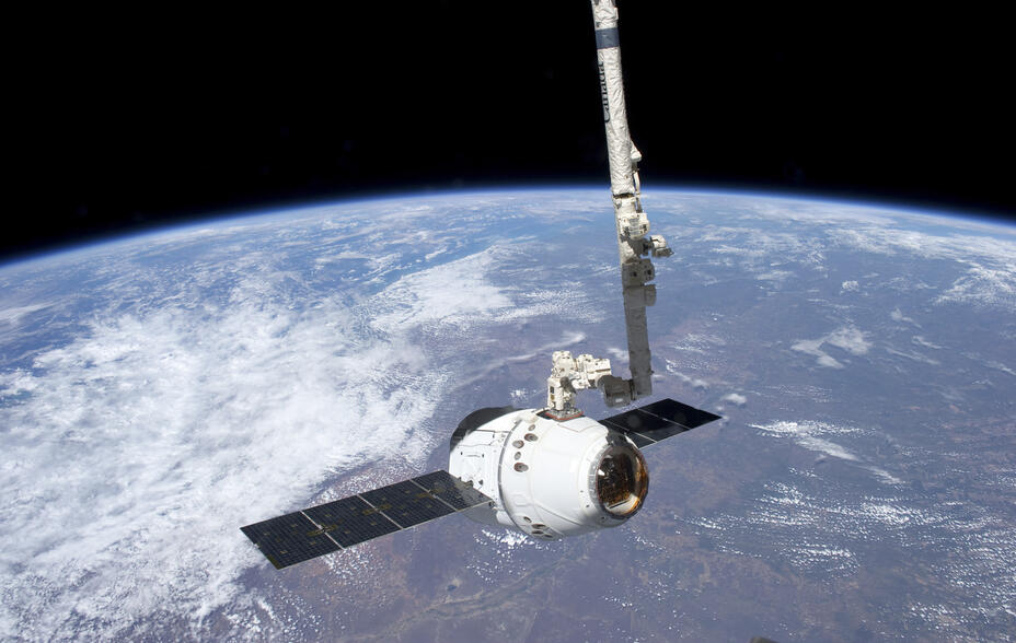 With clouds and land forming a backdrop, the SpaceX Dragon commercial cargo craft is grappled by the Canadarm2 robotic arm at the International Space Station.