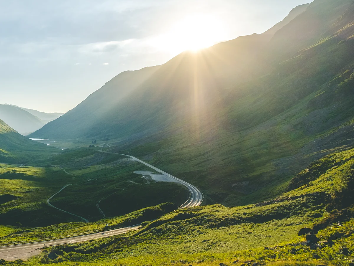 The sun shines above the mountain peaks of GLencoe, Scotland
