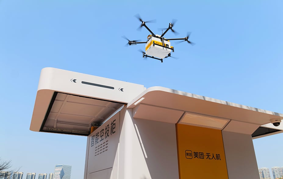 A Meituan drone flying above a delivery centre with a blue sky in the background