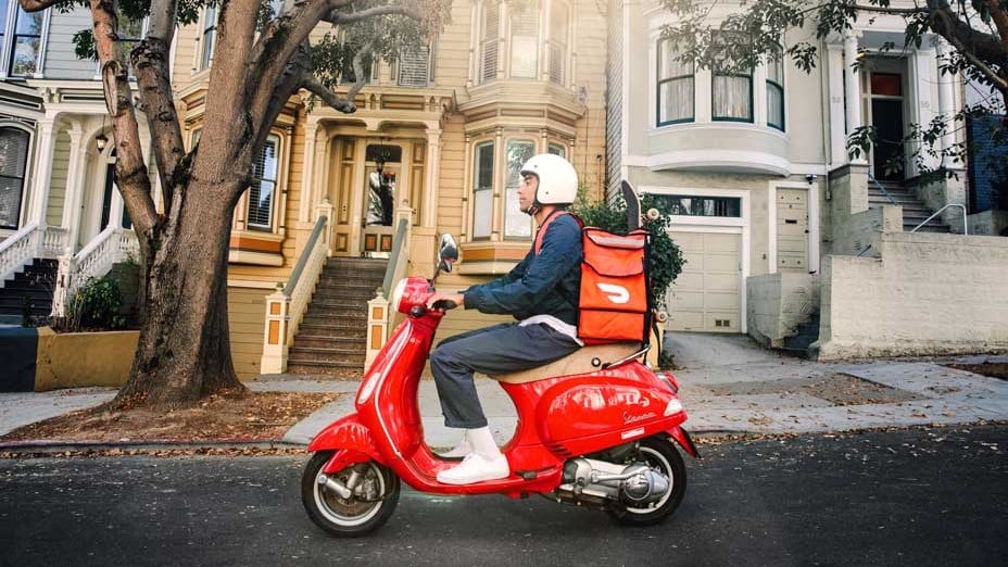 DoorDash rider on red moped and DoorDash branded delivery bag.