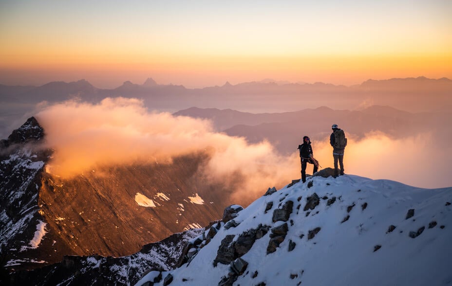 Silhouettes of hikers at sunrise on snowy mountain peak