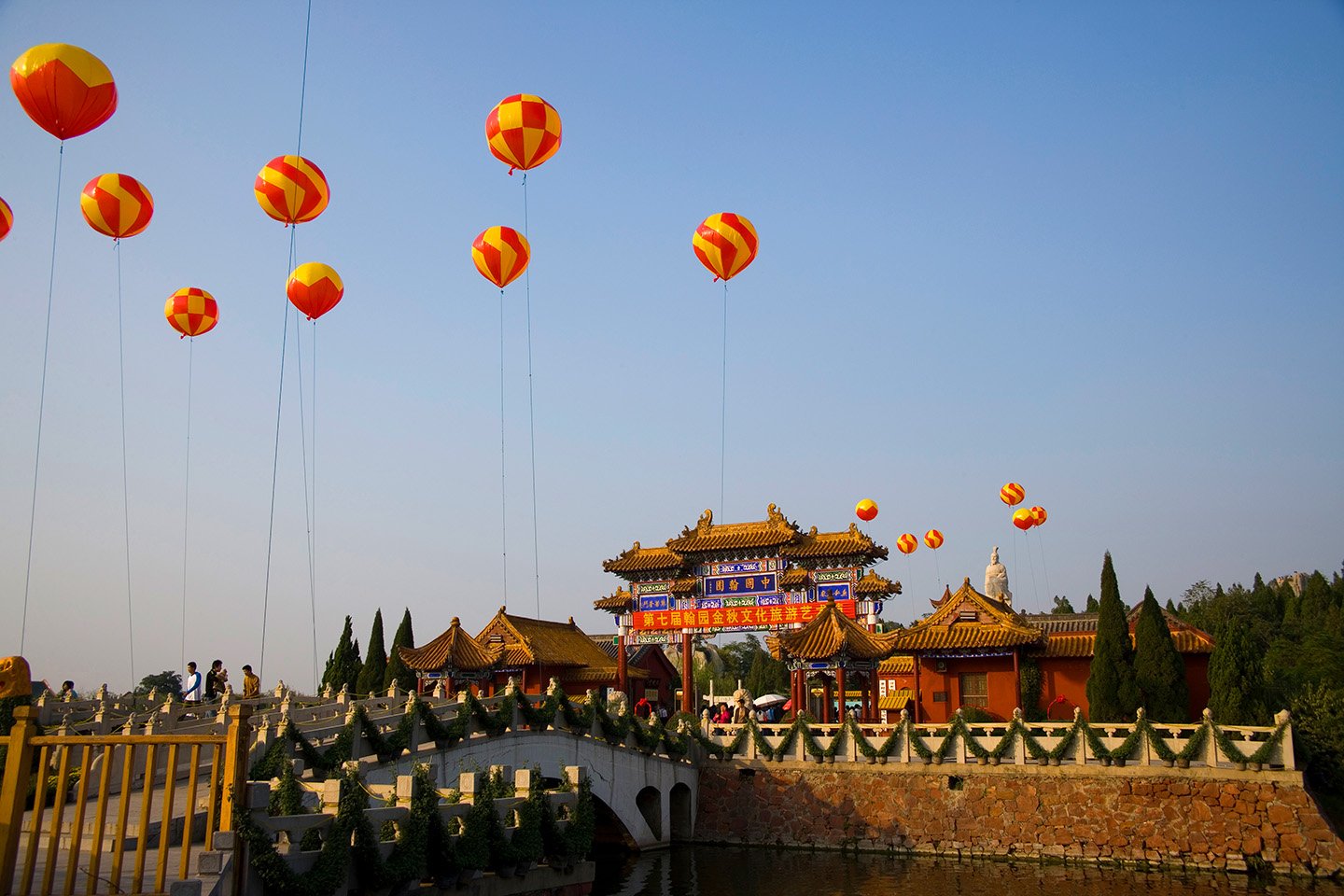 A coulourful and tradional architecture structure with yellow and red ballons floating above against a deep blue sky, in Henan province, China 