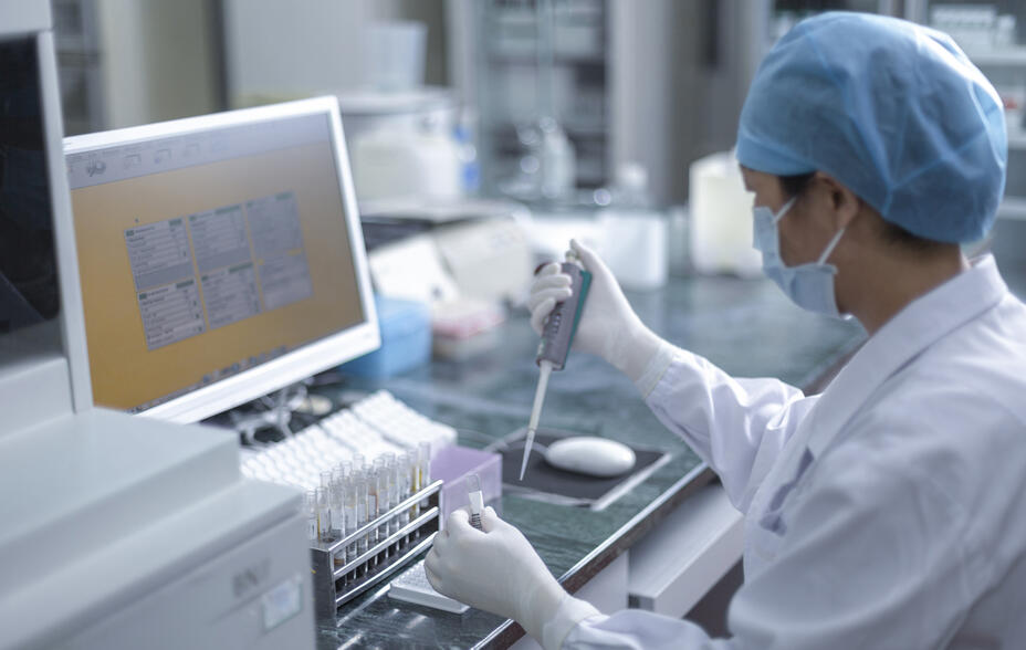 A worker in a Chinese pharmaceutical lab holds a pipette and a test tube.