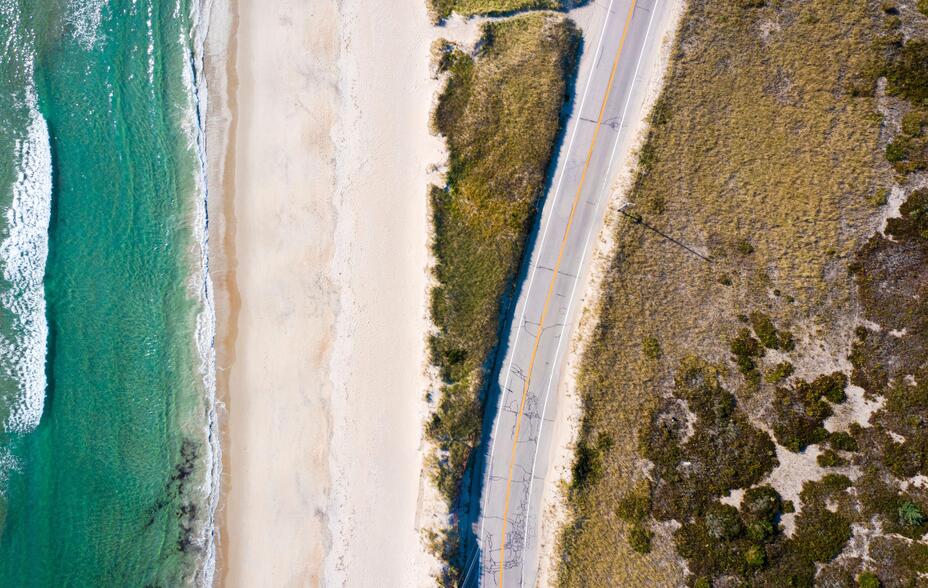 Aerial shot of a road and the ocean on a sandy beach shoreline.