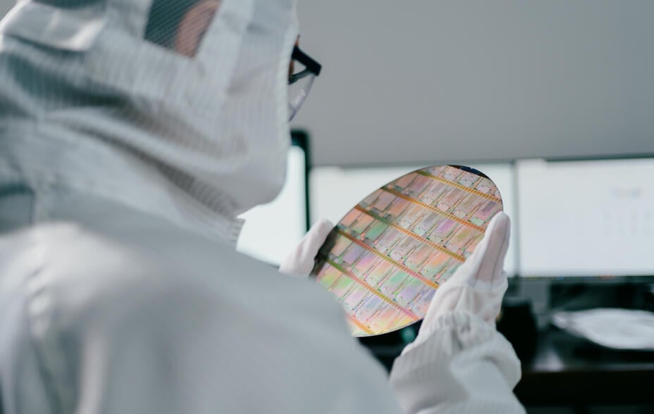 An employee wearing PPE carefully examines the microchips on a wafer