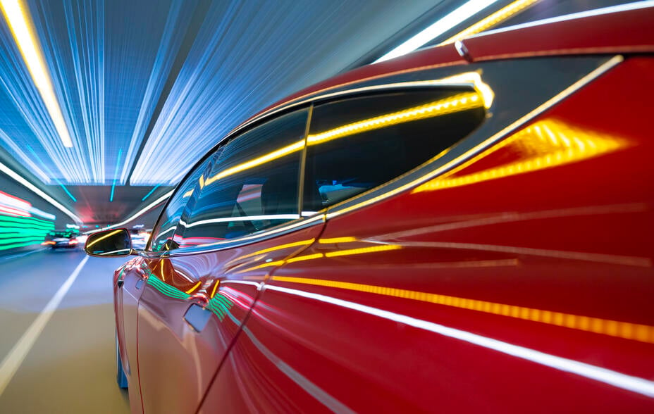 Red electric powered US car drives on city highway tunnel while night - streaking lights and road signs.