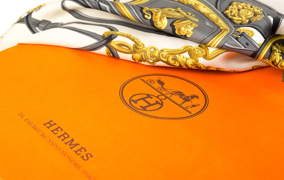 Orange Hermes gift box with white, gold and grey silk scarf draped over box