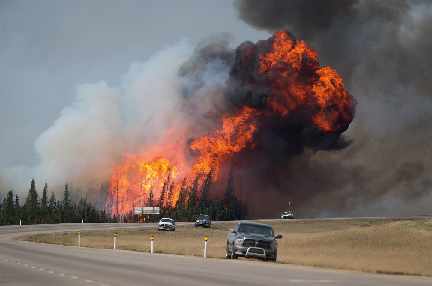 A wildfire burns behind abandoned vehicles on the Alberta Highway 63