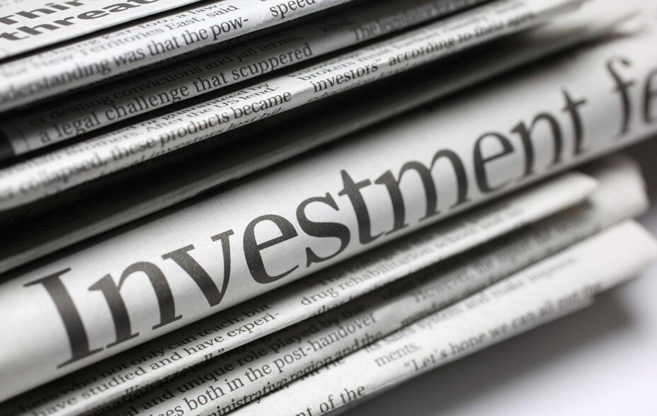 Photograph of a stack of folded newspapers with the word "Investment" prominently visible on one page.