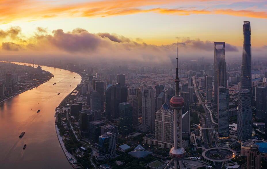 Shanghai's skyline. A sunset creates a golden sky as fluffy clouds hang over modern glass skyscrapers and the Hangpu river winds into the distance.