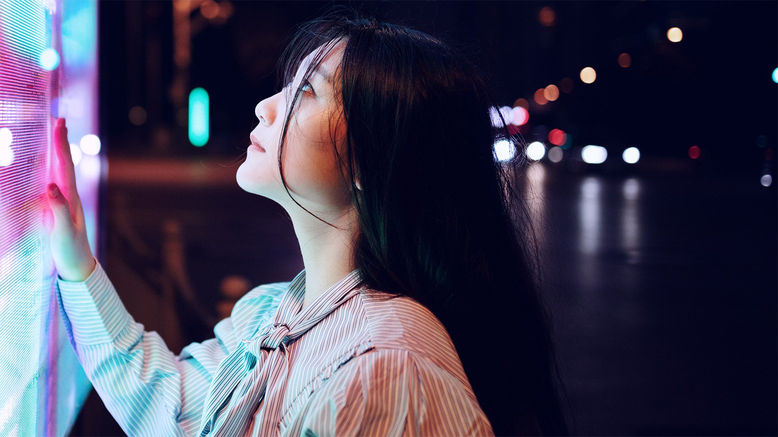 A person toucing a large multicoloured screen in a dark street in an Asian city